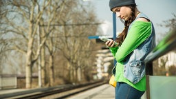 Junge Frau am Bahnhof schaut interessiert auf Handy.