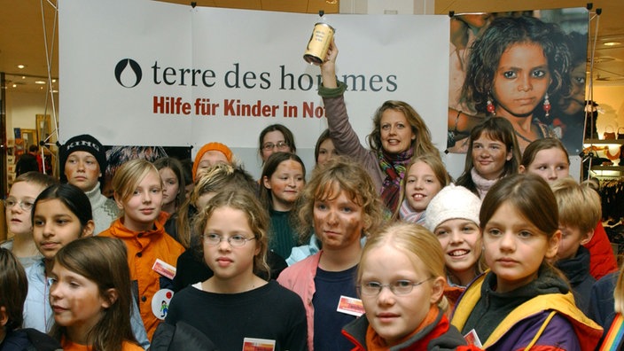 Die TV-Moderatorin Barbara Schöneberger hält bei einer vom Kinderhilfswerk "terre des hommes" inmitten von Kindern einen Sammelbecher hoch.