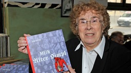 Toni Netzle stellt ihr Buch mein "alter Simpl" vor, hält ihr Buch in der hand und schaut ion die Kamera