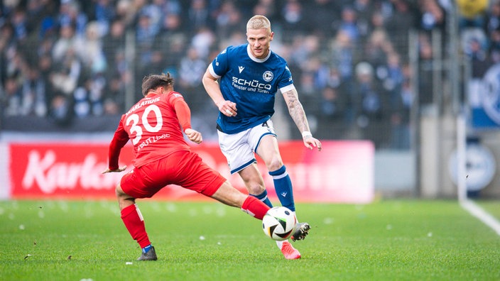 Bielefelds Louis Oppie wird beim Passversuch von Unterhachings Simon Skarlatidis gestört 