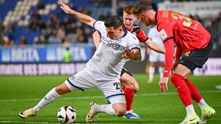 Stefano Russo von Arminia Bielefeld behauptet sich gegen Wiesbadens Felix Luckeneder (r) und Fabian Greilinger