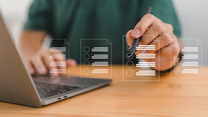 Ein tragbarer Computer steht auf einem Tisch, zwischen der Person und dem Computer werden virtuell symbolische Checklisten dargestellt.