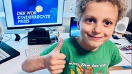 Junge hebt Daumen und sitzt am PC-Schreibtisch