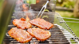 Das Bild zeigt vier Steaks auf einem Grill.