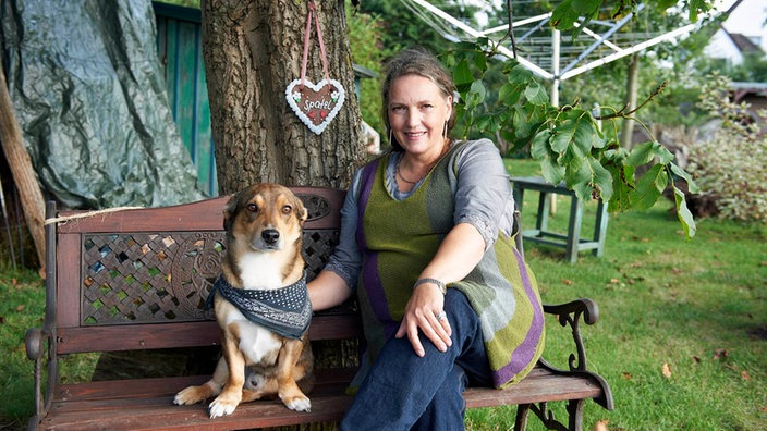 Anke sitzt mit Hund Feivel auf eienr Gartenbank unter einem Baum