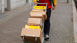 Das Bild zeigt einen Paketboten mit einer Sackkarre voller Pakete.