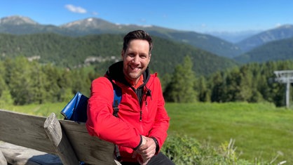 Das Bild zeigt Moderator Sven Kroll auf einer Bank in den Bergen in Kärnten.