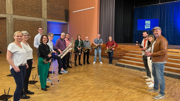 Das Bild zeigt Doc Esser mit der Big Band und ihren Instrumenten in einer Aula.