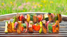 Das Bild zeigt einen Tisch mit gegrilltem Hähnchen, Steaks, Gemüse und einem Dip. 