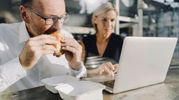 Das Bild zeigt einen Mann beim schnellen Mittagessen vor dem Computer.