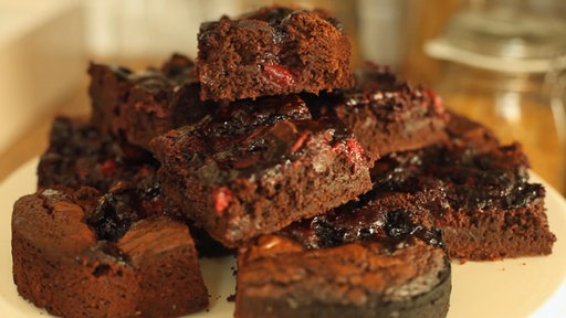 Viele Stücke Brownies auf einem Teller, auf den Brownies ist rote Grütze