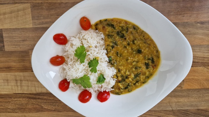 Linsencurry mit Spinat und Tomaten dekoriert auf einem weißen Teller.