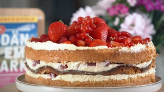 Die Fru-Pigalopp-Torte mit Blumen und Reiseführer im Hintergrund.