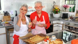 Martina und Moritz stehen in der Küche und probieren Apfelkuchen vom Blech