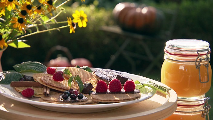 Honigwaffeln mit Beeren auf einem Teller, daneben ein Glas Honig