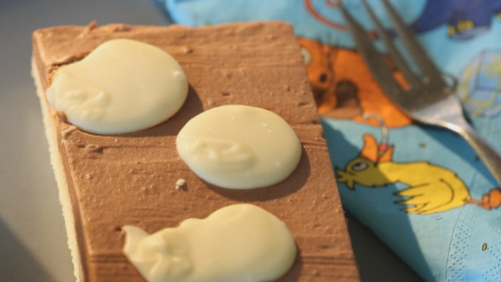 Ein Stück Kuchen in der Form eines Quaders. Auf dem Kuchen sind weiße Flecken. Rechts neben dem Kuchen liegt eine Gabel.