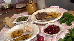 Zwei Teller mit Bratkartoffeln und Wurst sowie Schalen mit Roter Bete und Gurken