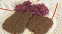 Zwei Rehschnitzel mit Fichtennadelkruste und Rotkohl auf einem Teller angerichtet