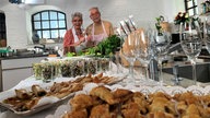 Martina und Moritz stehen hinter einem Tisch mit Häppchen und Tapas für das Silvesterbuffet