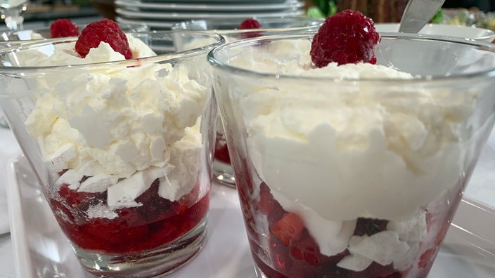 Zwei Gläser gefüllt mit Himbeeren und Baiser, gekrönt von einer Himbeere