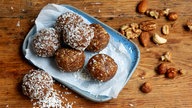 Das Bild zeigt Energiebällchen mit Nüssen und Trockenobst auf einem kleinen rechteckigen Teller.