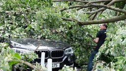 Ein Anwohner versucht, sein Auto von Ästen zu befreien