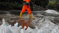 Ein Arbeiter geht in Bad Münstereifel hinter einer Wassersperre aus Sandsäcken über eine durch den Fluss Erft überschwemmte Straße